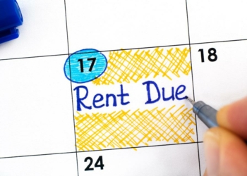 Woman fingers with blue pen writing reminder Rent Due in calendar.