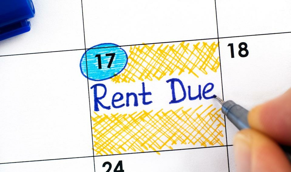 Woman fingers with blue pen writing reminder Rent Due in calendar.