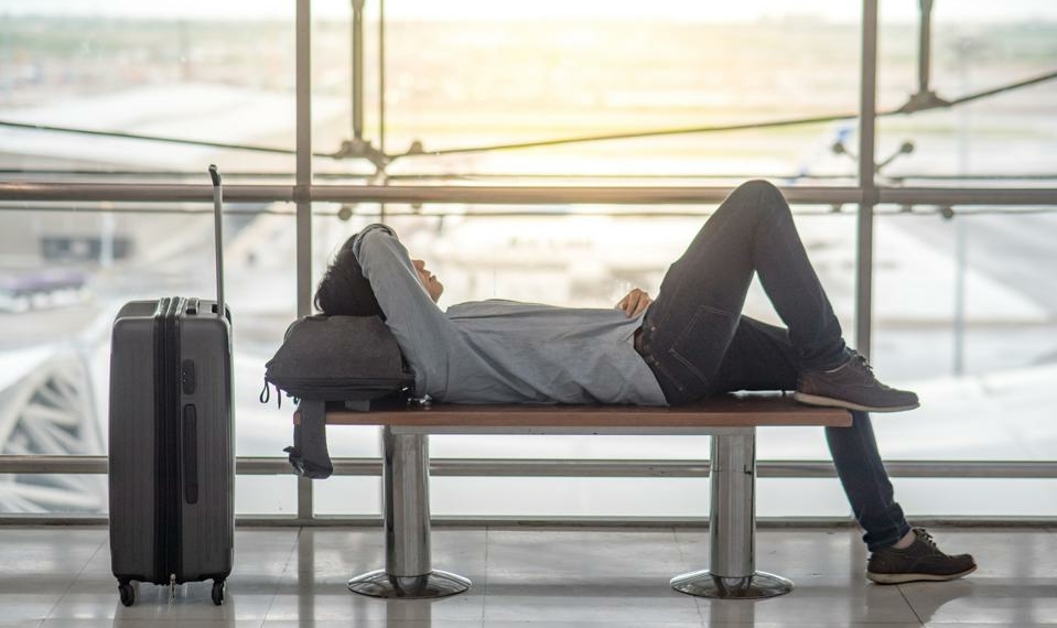 Young Asian man with suitcase luggage and backpack lying on bench in airport terminal