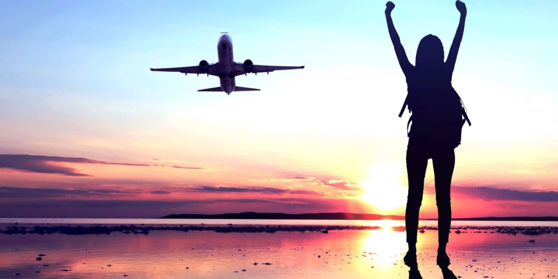 Brokers favorite ASX share COVID reopening trade buyA woman standing on a tarmac celebrates a plane lifting off, indicating rising share price in ASX travel companies