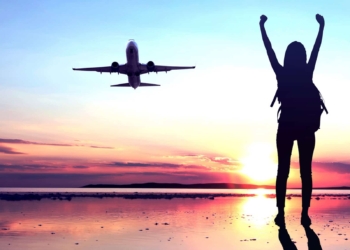 Brokers favorite ASX share COVID reopening trade buyA woman standing on a tarmac celebrates a plane lifting off, indicating rising share price in ASX travel companies