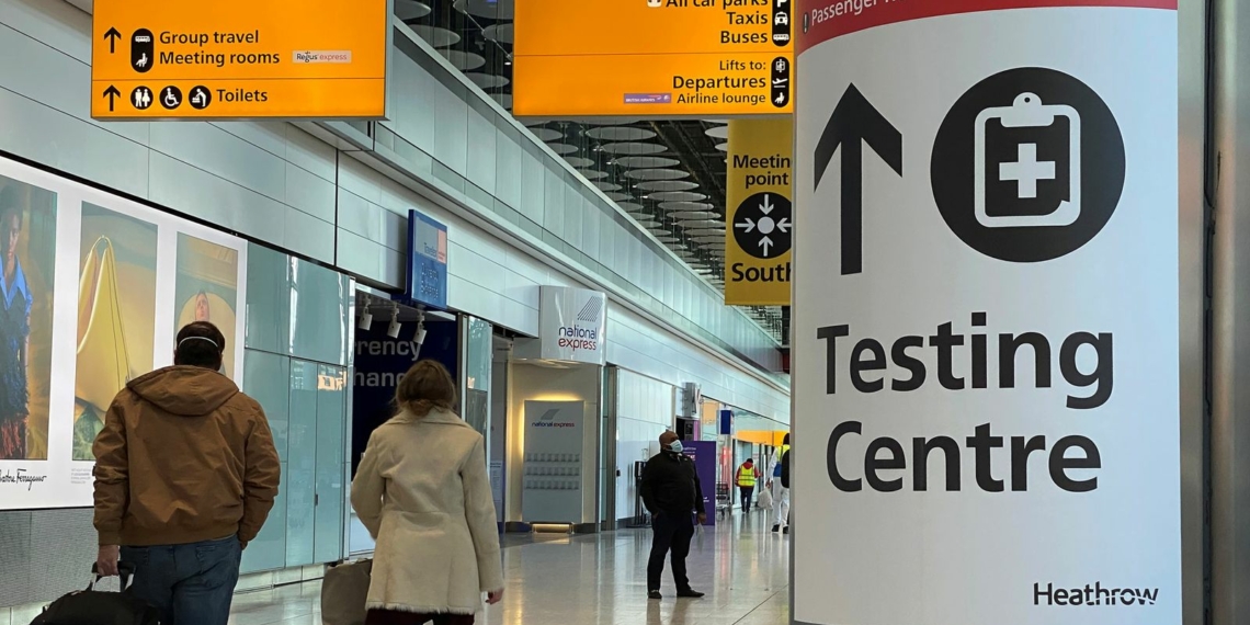 Travellers pass a sign for a COVID-19 test centre at Heathrow Airport