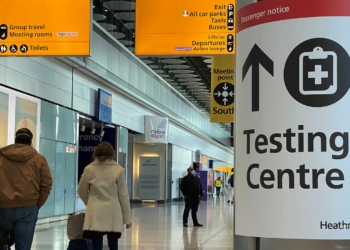 Travellers pass a sign for a COVID-19 test centre at Heathrow Airport