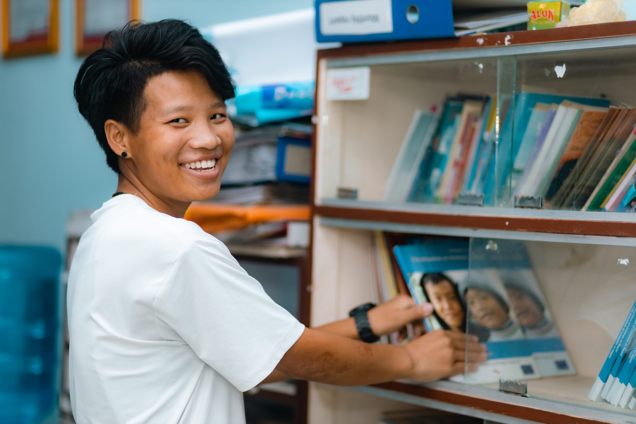 Tansuwa is picking a book from a shelf. 