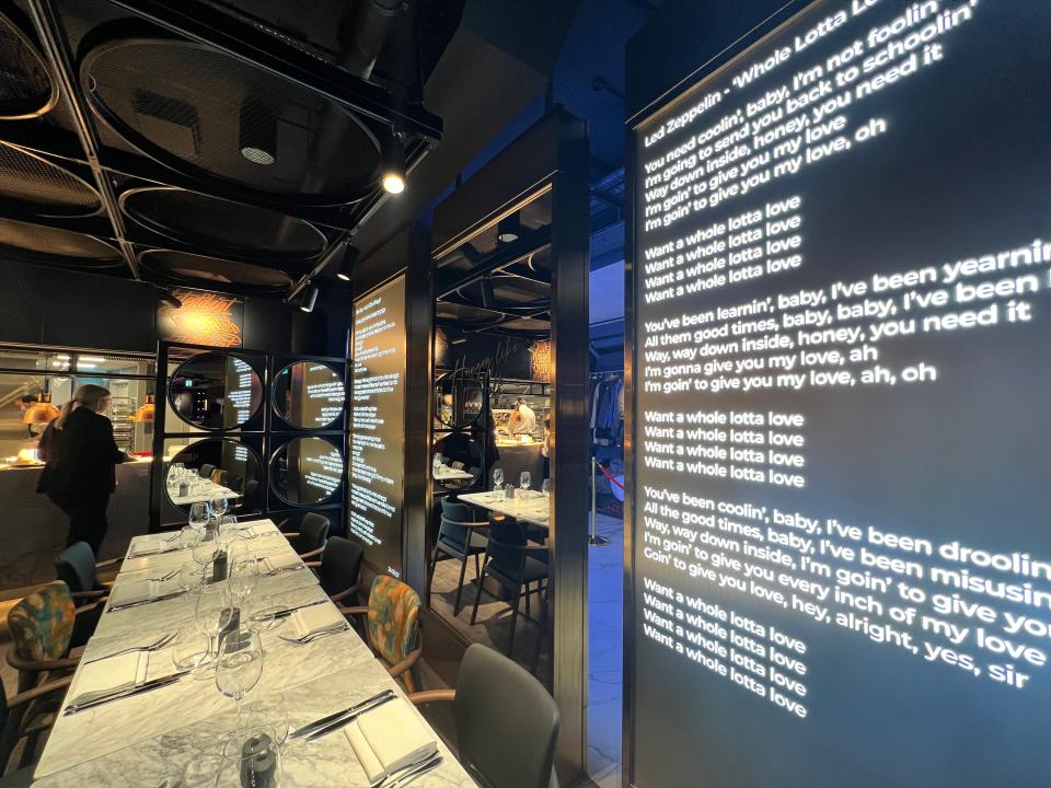 A LED display of Led Zeppelin lyrics in white on black next to dining tables laid out with cutlery in The NinetyThird