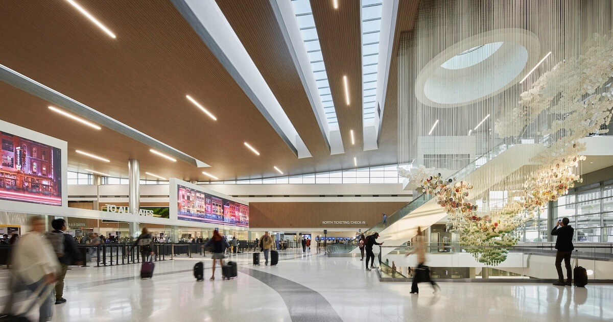 Spacious airport terminal interior with travelers, digital displays, and a decorative hanging installation.