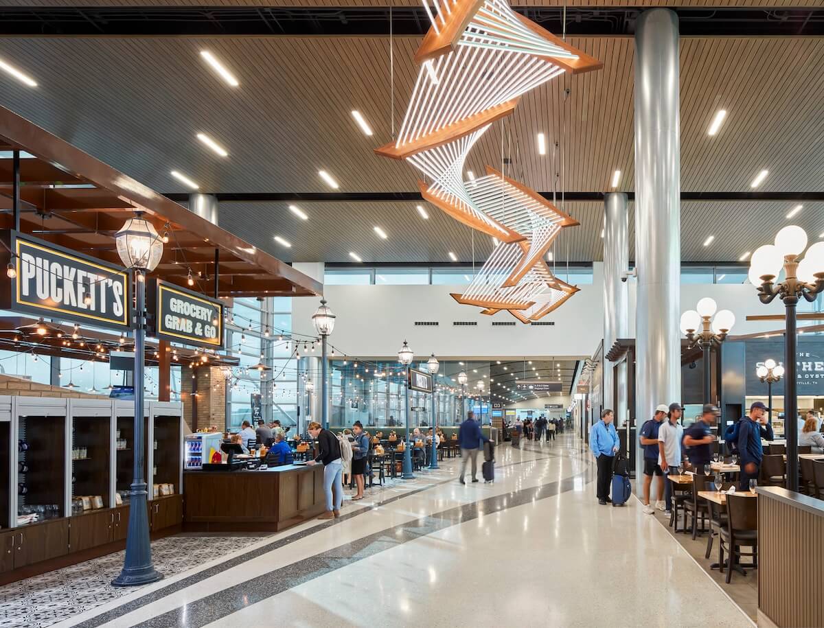 Modern airport terminal with travelers, dining areas, and distinctive overhead lighting.